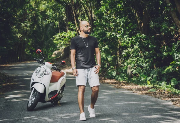 Şık bir genç adam ve motosikleti ormanda yolda.