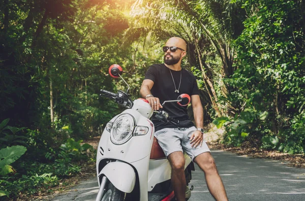 Şık bir genç adam ve motosikleti ormanda yolda.
