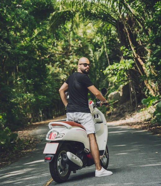 Şık bir genç adam ve motosikleti ormanda yolda.