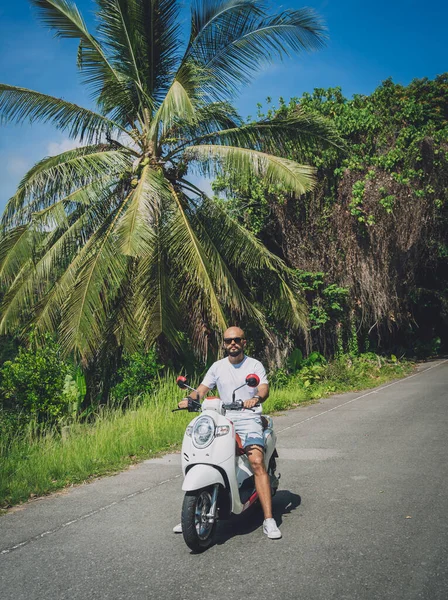 Şık bir genç adam ve motosikleti ormanda yolda.