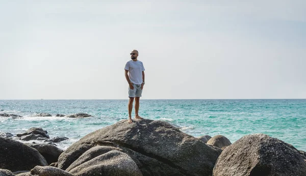 Ung man kopplar av på stranden när han står på en sten — Stockfoto