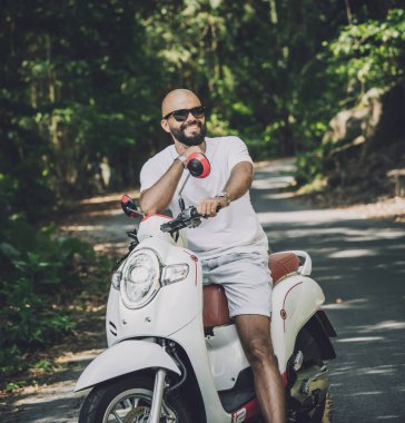 Şık bir genç adam ve motosikleti ormanda yolda.