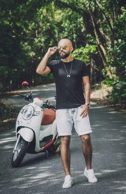 Şık bir genç adam ve motosikleti ormanda yolda.