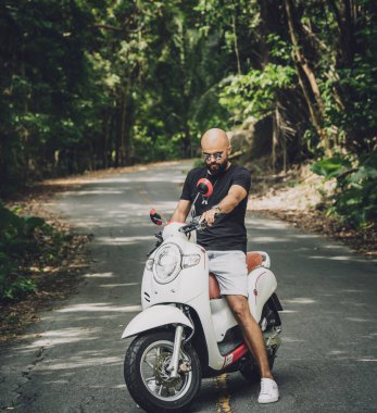 Şık bir genç adam ve motosikleti ormanda yolda.