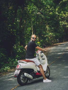 Şık bir genç adam ve motosikleti ormanda yolda.