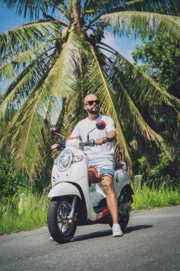 Şık bir genç adam ve motosikleti ormanda yolda.