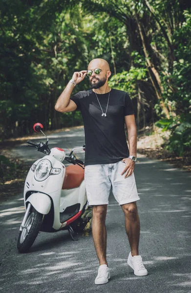 Şık bir genç adam ve motosikleti ormanda yolda.