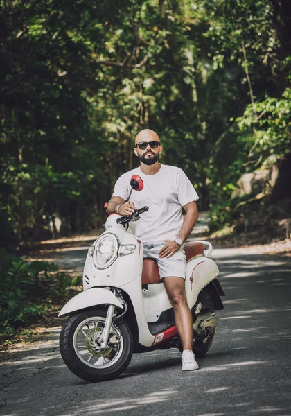 Şık bir genç adam ve motosikleti ormanda yolda.