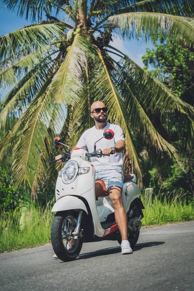 Şık bir genç adam ve motosikleti ormanda yolda.