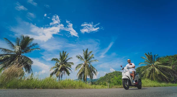 Стильний молодий чоловік їде на мотоциклі по дорозі біля моря і пальми — стокове фото
