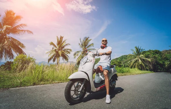 Elegante joven monta una moto en la carretera cerca del mar y las palmeras —  Fotos de Stock