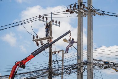 Elektrikçiler elektrik direğindeki yüksek voltajlı kabloları tamir ediyorlar.