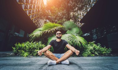 Genç adam ormanda güzel yeşil yapraklarla yoga yapıyor.