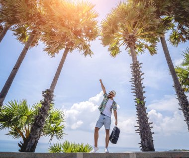 Yaz tatilinde arka planda güzel palmiyeler ve deniz manzaraları olan genç bir gezgin.