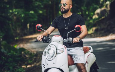 Şık bir genç adam ve motosikleti ormanda yolda.