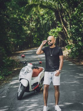 Şık bir genç adam ve motosikleti ormanda yolda.