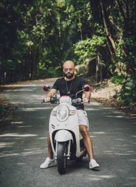 Şık bir genç adam ve motosikleti ormanda yolda.
