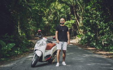 Şık bir genç adam ve motosikleti ormanda yolda.