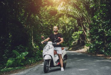 Şık bir genç adam ve motosikleti ormanda yolda.