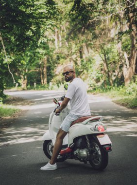 Şık bir genç adam ve motosikleti ormanda yolda.