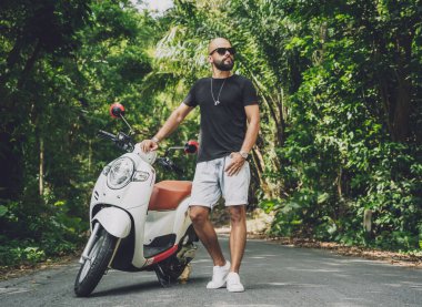 Şık bir genç adam ve motosikleti ormanda yolda.