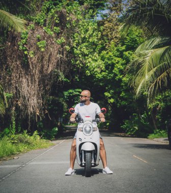 Şık bir genç adam ve motosikleti ormanda yolda.