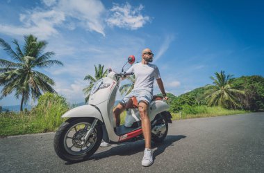 Şık bir genç adam deniz kenarında motosiklet sürüyor ve palmiye ağaçları.