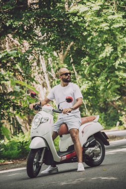 Şık bir genç adam ve motosikleti ormanda yolda.