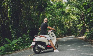 Şık bir genç adam ve motosikleti ormanda yolda.