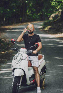 Şık bir genç adam ve motosikleti ormanda yolda..