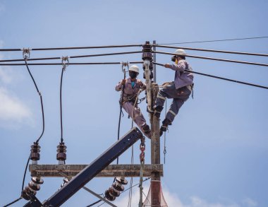 Electricians is repairing high voltage wires on electric power pole.