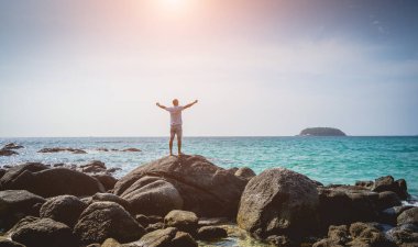 Genç adam sahilde dinlenirken bir taşın üzerinde duruyor..