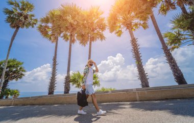 Yaz tatilinde arka planda güzel palmiyeler ve deniz manzaraları olan genç bir gezgin..
