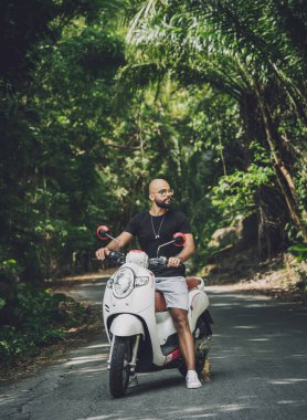 Şık bir genç adam ve motosikleti ormanda yolda..