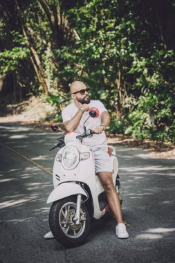 Şık bir genç adam ve motosikleti ormanda yolda..