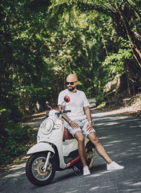 Şık bir genç adam ve motosikleti ormanda yolda..