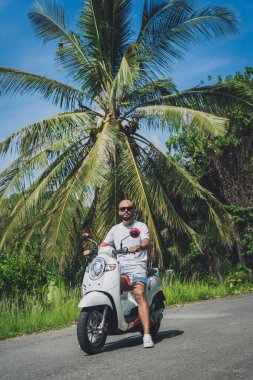 Şık bir genç adam ve motosikleti ormanda yolda..