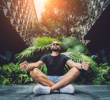 Genç adam ormanda güzel yeşil yapraklarla yoga yapıyor..