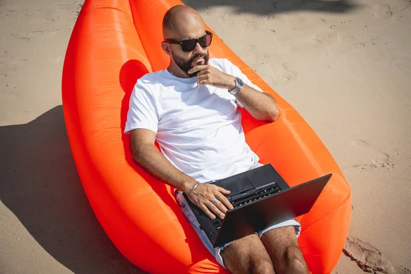 Genç Adam Şişme Bir Koltukta Otururken Kumsalda Dizüstü Bilgisayarıyla Çalışıyor — Stok fotoğraf