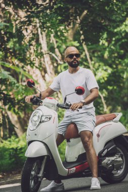 Şık bir genç adam ve motosikleti ormanda yolda..