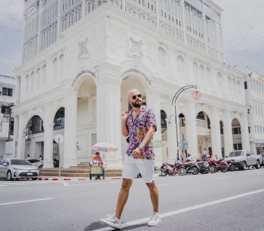 Genç bir adam sırt çantasıyla bir Asya şehrinin caddesinde seyahat ediyor..