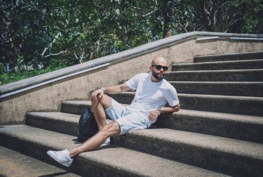 Yalnız genç yakışıklı adam parkta merdivenlerde oturuyor..