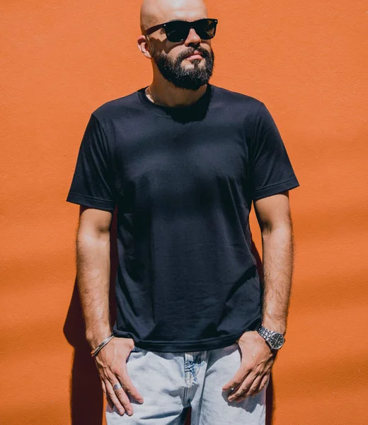 Male model with beard wearing black blank t-shirt on the background of an orange wall.