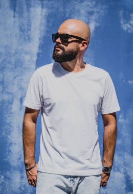 Mavi bir duvarın arkasında beyaz tişört giyen sakallı bir erkek model..