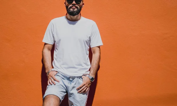Male model with beard wearing white blank t-shirt on the background of an orange wall.