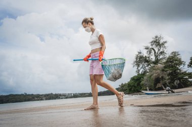 Kadın bir çevre bilimci plastikten ve diğer atıklardan sahil kenarını temizliyor..