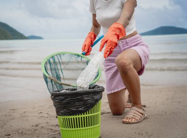 A female ecologist volunteer cleans the beach on the seashore from plastic and other waste.