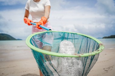 A female ecologist volunteer cleans the beach on the seashore from plastic and other waste.