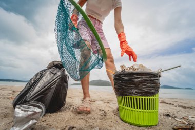 Kadın bir çevre bilimci plastikten ve diğer atıklardan sahil kenarını temizliyor..