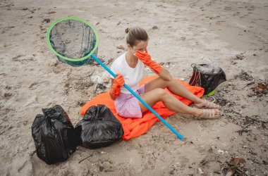 A female ecologist volunteer is resting after cleaning the beach on the seashore from plastic and other waste.